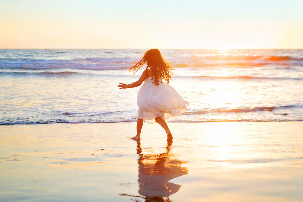 Little girl in white dress running on the beach in Carlsbad, California for her photo session with Kristin Rachelle Photography