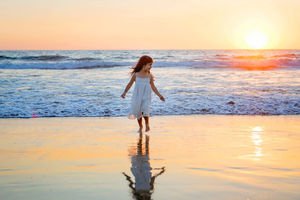Little girl in white dress running on the beach in Carlsbad, California for her photo session with Kristin Rachelle Photography